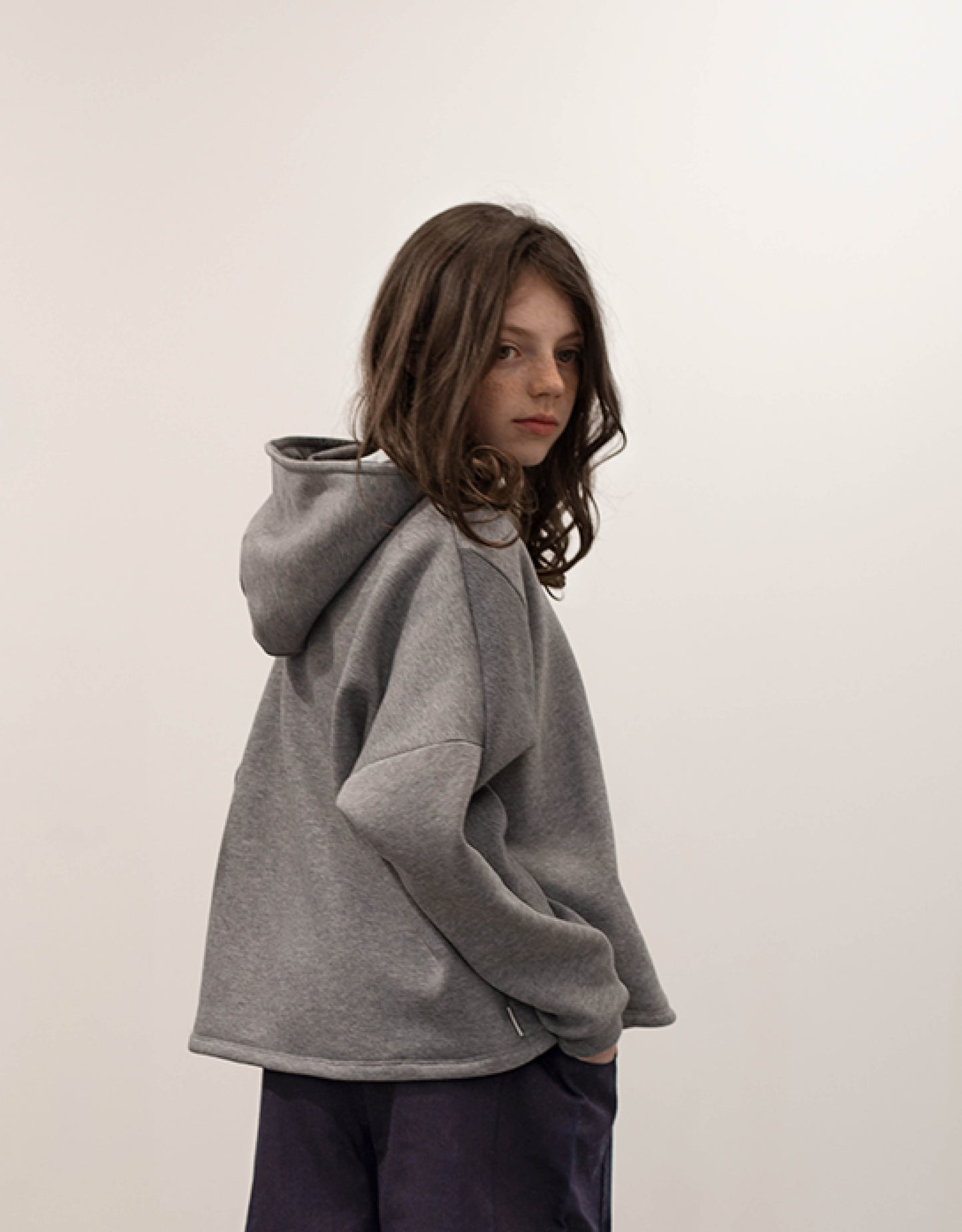 Hoodie pour enfant, gris, coupe droite oversized, emmanchures basses, découpes asymétriques. Upcyclé et unisexe. Made in France. Kid, hoodie, grey, oversized straight cut, low armholes, asymmetrical lines. Upcycled and unisex. Made in France.