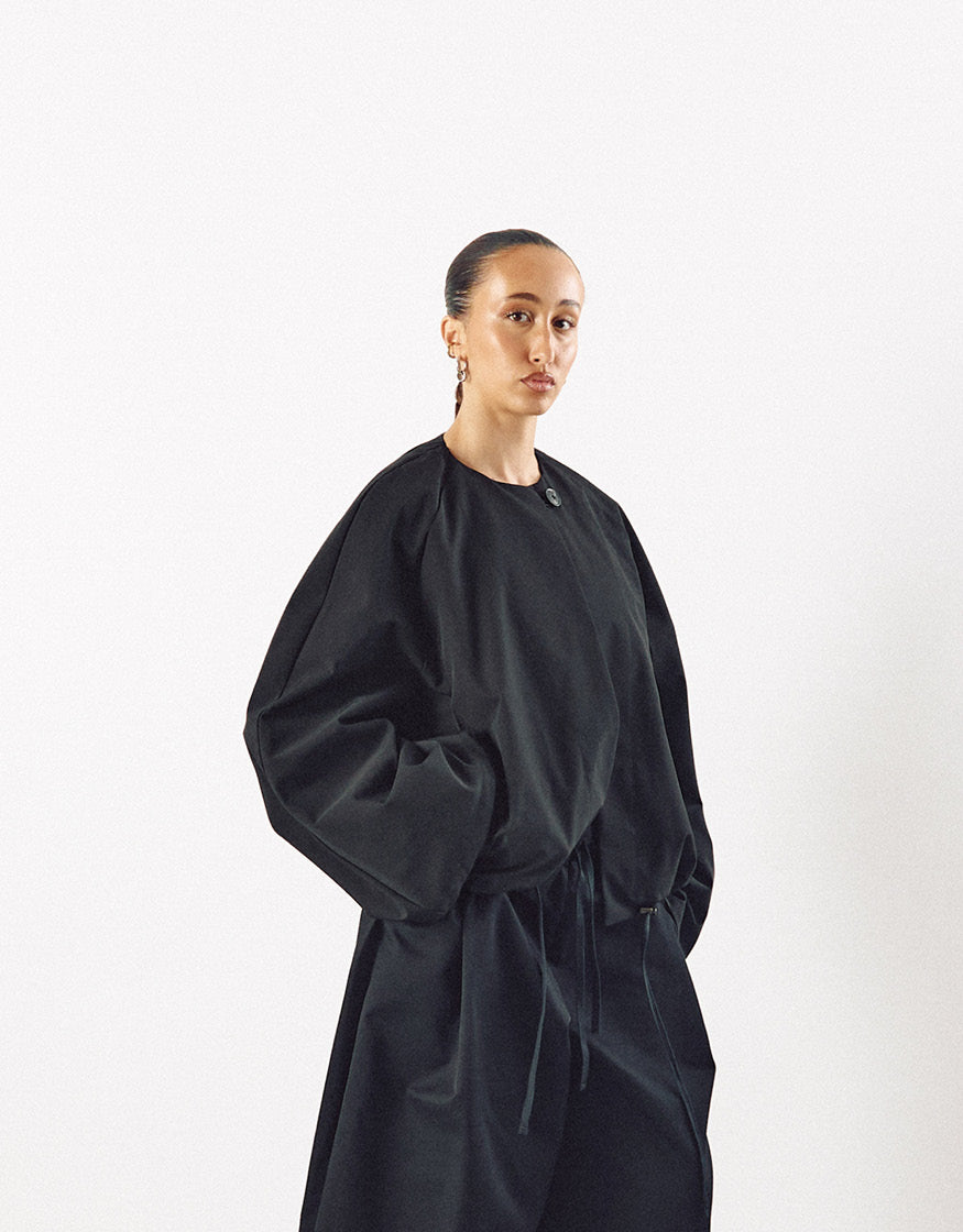 Model wearing a minimalist black jacket with an oversized silhouette and pockets, featuring understated elegance and high-quality craftsmanship.