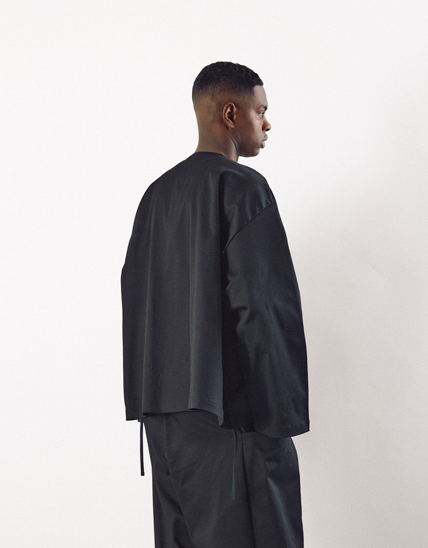 Profile view of a man wearing a minimalist black oversized kimono-style top paired with matching loose pants, emphasizing clean lines and understated elegance.