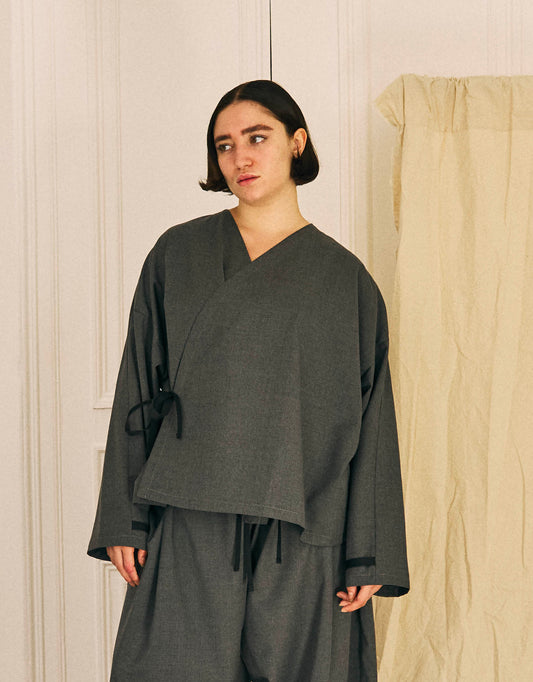 Unisex kimono, straight cut, oversized, low armholes, quilted strap at bottom of sleeves to modify volume, asymmetrical lines, cross-over front, closes with cotton taffeta ties of different widths. Designed to be worn both closed and open as an overshirt.
Made in France, in a Storm Grey light, fluid and crease resistant suiting, 65% Polyester, 35% Wool, 198g/m², from a fashion house's dead stock.