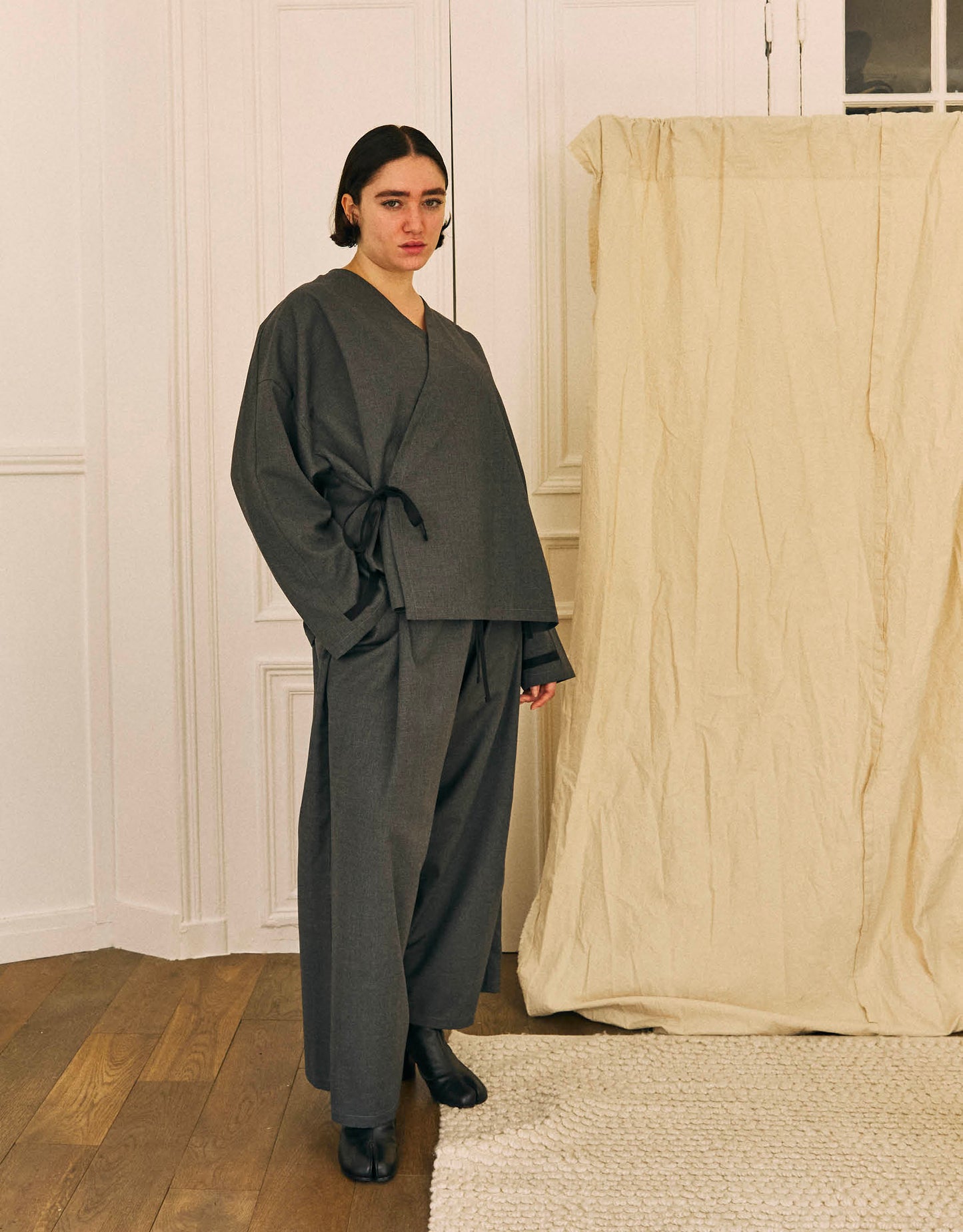 Unisex kimono, straight cut, oversized, low armholes, quilted strap at bottom of sleeves to modify volume, asymmetrical lines, cross-over front, closes with cotton taffeta ties of different widths. Designed to be worn both closed and open as an overshirt.
Made in France, in a Storm Grey light, fluid and crease resistant suiting, 65% Polyester, 35% Wool, 198g/m², from a fashion house's dead stock.