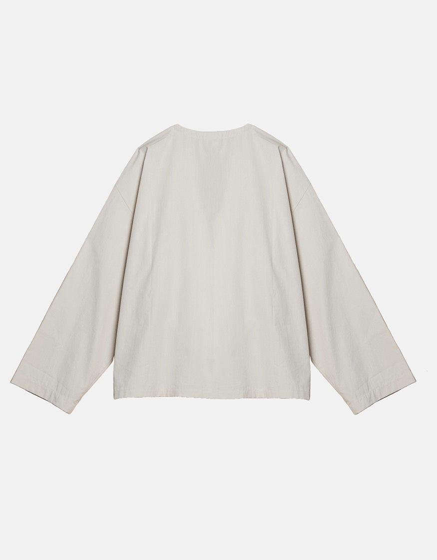 Off-white minimalist kimono-style top with wide sleeves and clean lines, emphasizing understated elegance and contemporary unisex design.