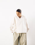 Model wearing an off-white minimalist kimono-style top with wide sleeves and a wrap detail, paired with loose, light beige trousers, showcasing understated elegance and volume.