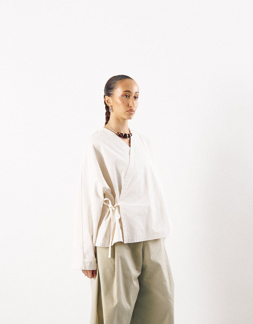 Model wearing an off-white minimalist kimono-style top with a wrap detail paired with loose, light-colored trousers, showcasing understated elegance and contemporary design.