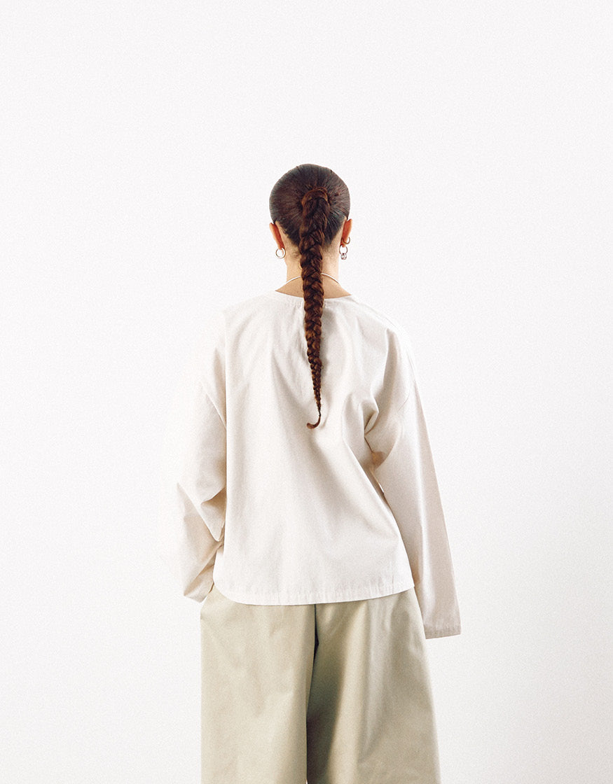 Back view of a model wearing an off-white minimalist kimono-style top paired with loose, neutral-toned pants, showcasing understated elegance and relaxed volume.
