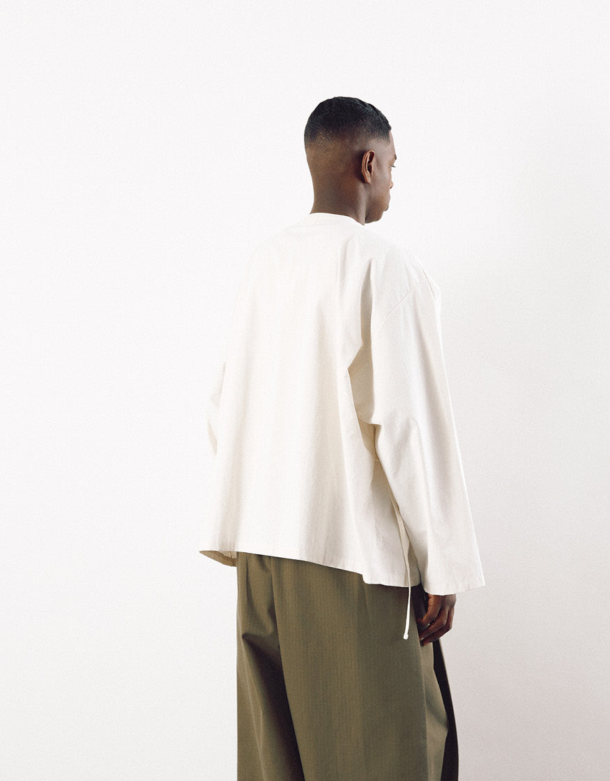 Model wearing an off-white minimalist oversized top with long sleeves paired with loose olive green trousers, showcasing subtle asymmetry and clean lines.