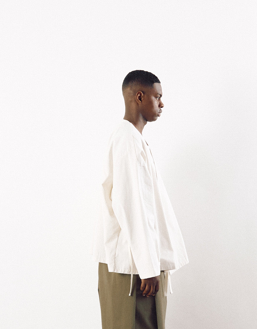 Profile view of a model wearing an off-white minimalist kimono-inspired jacket with loose volume, paired with olive green trousers, showcasing contemporary unisex design.