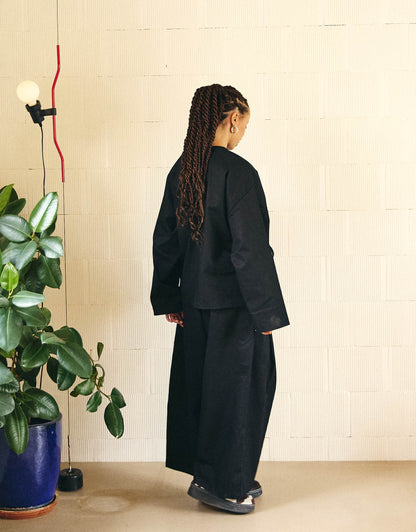 Unisex kimono, straight cut, oversized, low armholes, quilted strap at the bottom of the sleeves to modify volume, asymmetrical lines, cross-over front, closes with cotton taffeta ties of different widths. Designed to be worn both closed and open as an overshirt.
Made in France, in a Black stretch cotton gabardine, 98% Cotton, 2% Elastane, 251g/m², from a fashion house's dead stock.