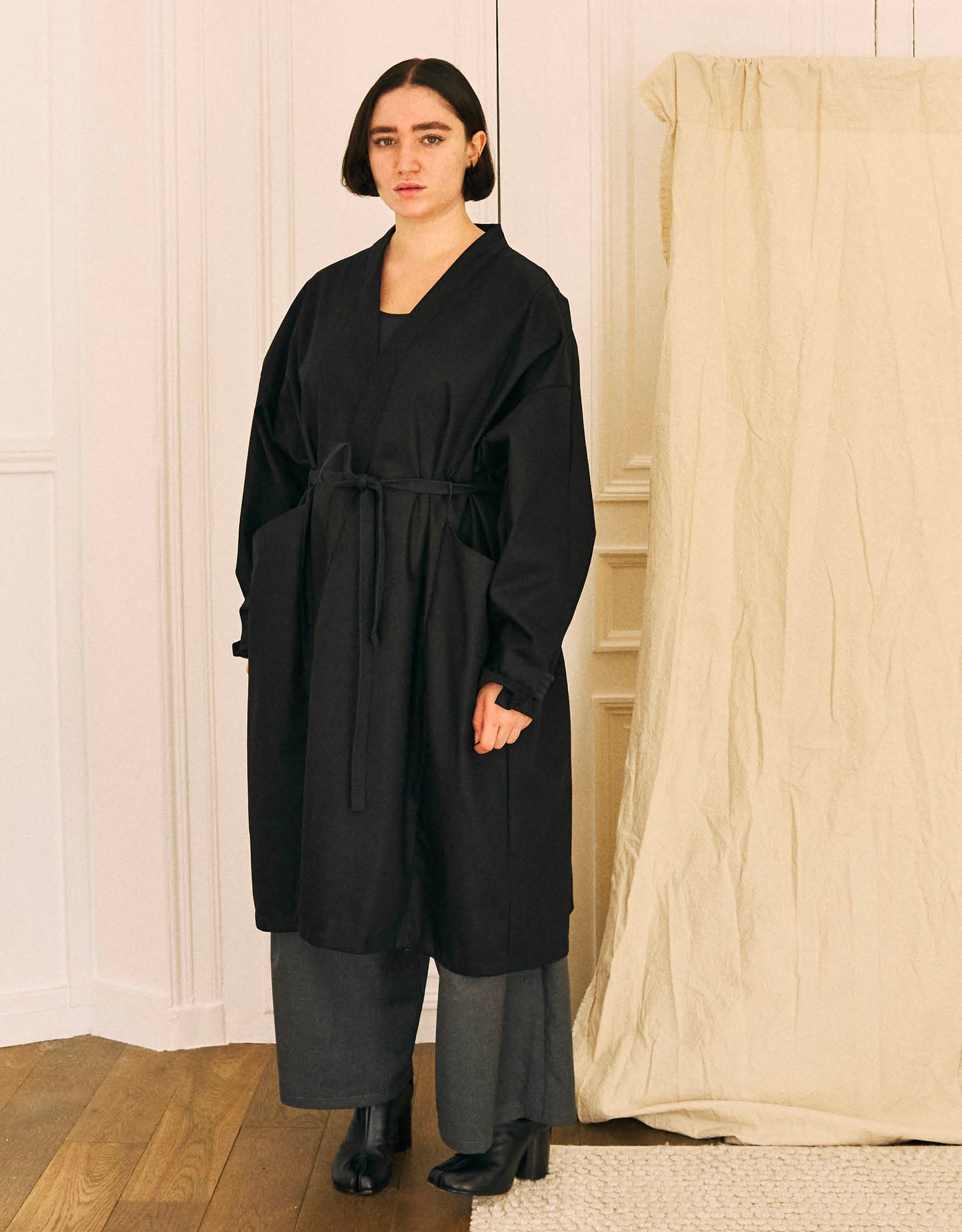 Unisex light coat, straight cut, oversized, low armholes, quilted strap at bottom of sleeves to modify volume, two wide pockets, asymmetrical lines, two wide pleats in back, cross-over front, closed by a belt.
Made in France, in a Black stretch cotton gabardine, 98% Cotton, 2% Elastane, 251g/m², from a fashion house's dead stock.