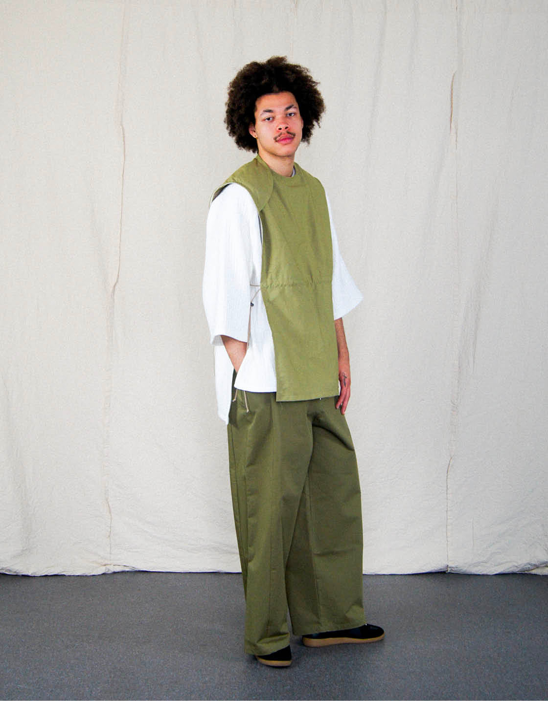 Pantalon - Chapitre 1, unisexe, jambes amples et droites, deux poches latérales, ceinture élastiquée, ajustable avec un cordon, dans un sergé de coton Olive. Pants - Chapter 1, unisex, wide, straight legs, two side pockets, elastic waistband, adjustable with drawstring, in Olive cotton twill.