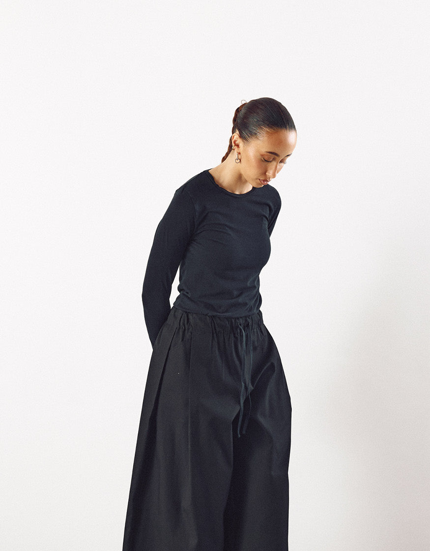 Woman wearing minimalist black wide pants with a drawstring waist paired with a fitted black long-sleeve top, showcasing contemporary unisex design and understated elegance.