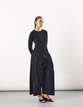 Woman wearing wide black pants with a drawstring waist paired with a fitted long-sleeve top, showcasing minimalist and contemporary style with comfortable volume and movement.