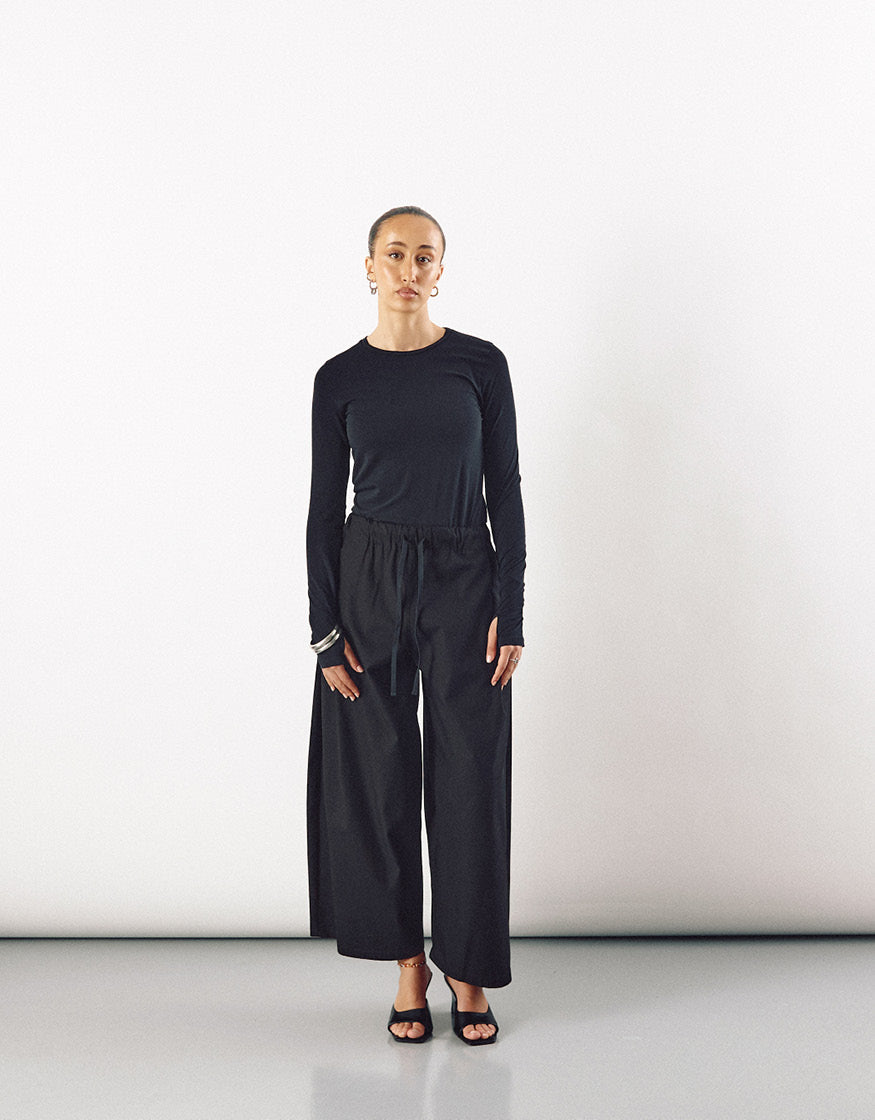 Model wearing minimalist black wide pants with a relaxed silhouette paired with a fitted long-sleeve top, showcasing understated elegance and contemporary design.