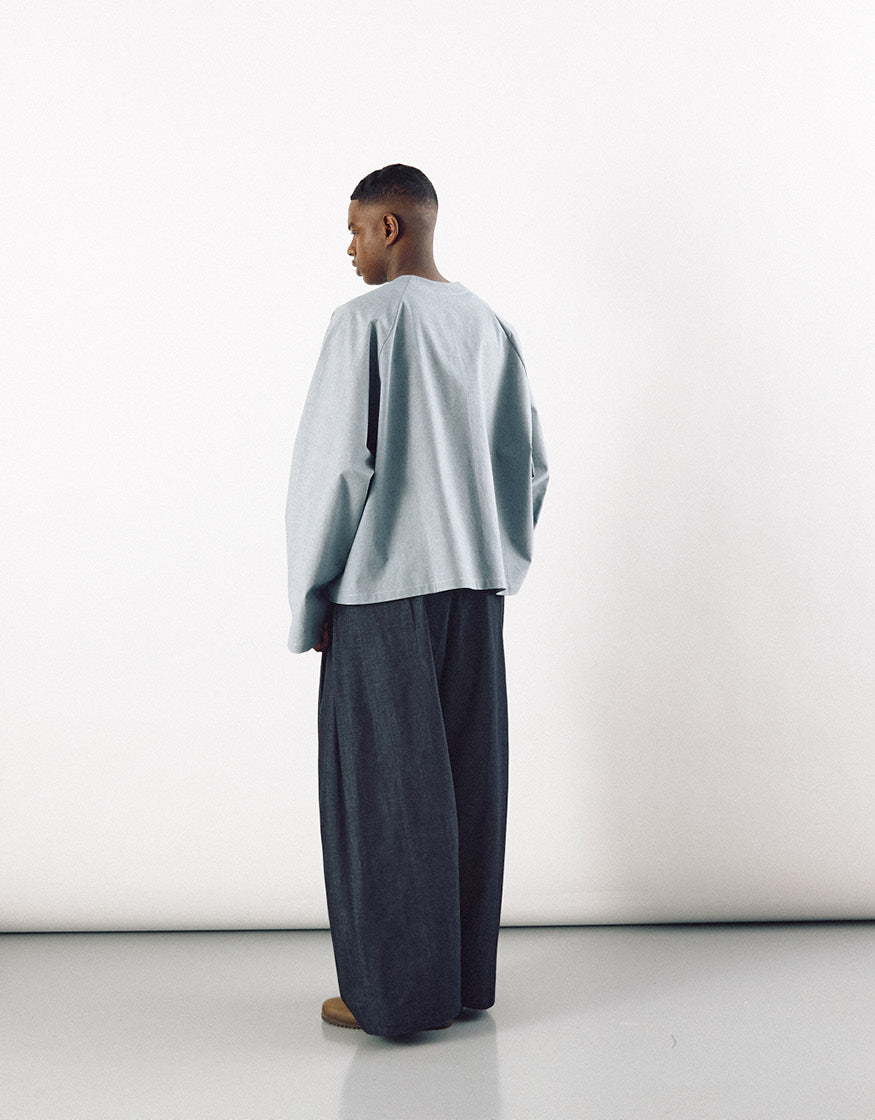 Model wearing loose-fitting indigo wide pants paired with a light grey oversized top, showcasing minimalist unisex fashion with emphasis on volume and understated elegance.