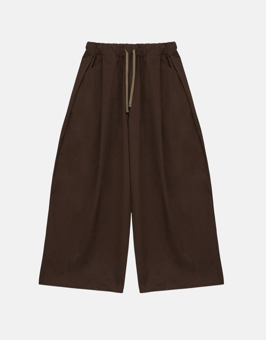 Minimalist unisex wide pants in tobacco color featuring a relaxed fit, elastic waistband with drawstrings, and subtle volume for effortless movement and understated elegance.