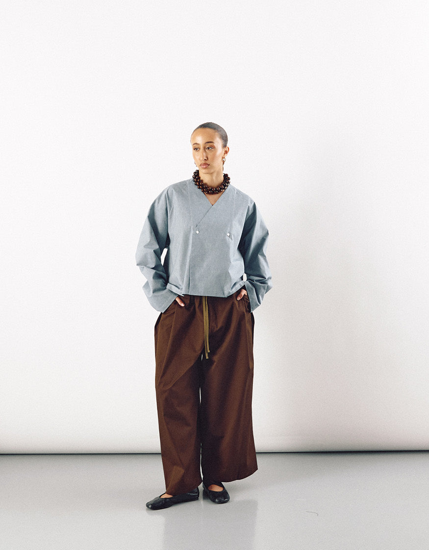 Model wearing contemporary unisex wide tobacco-colored pants paired with a minimalist light blue top, showcasing understated elegance and relaxed silhouette.