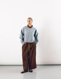 Model wearing contemporary unisex wide tobacco-colored pants paired with a minimalist light blue top, showcasing understated elegance and relaxed silhouette.