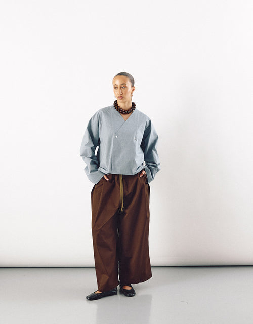 Model wearing contemporary unisex wide tobacco-colored pants paired with a minimalist light blue top, showcasing understated elegance and relaxed silhouette.