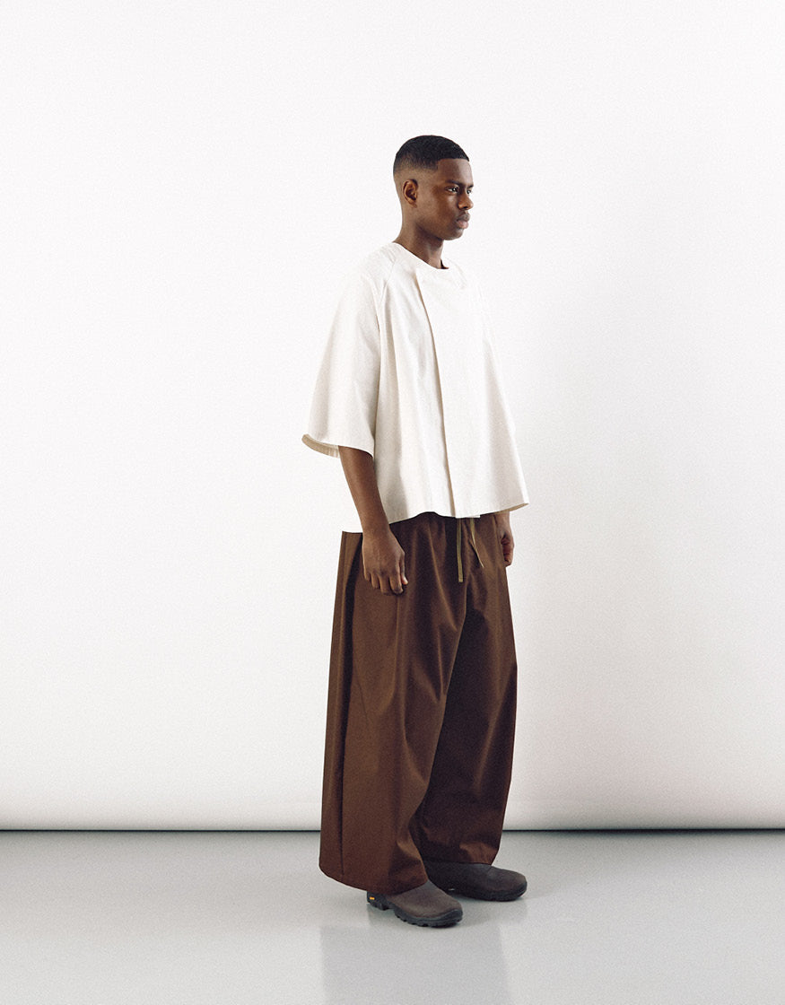 Male model wearing tobacco-colored wide pants paired with a loose, cream-colored top, showcasing minimalist design and relaxed volume for freedom of movement.