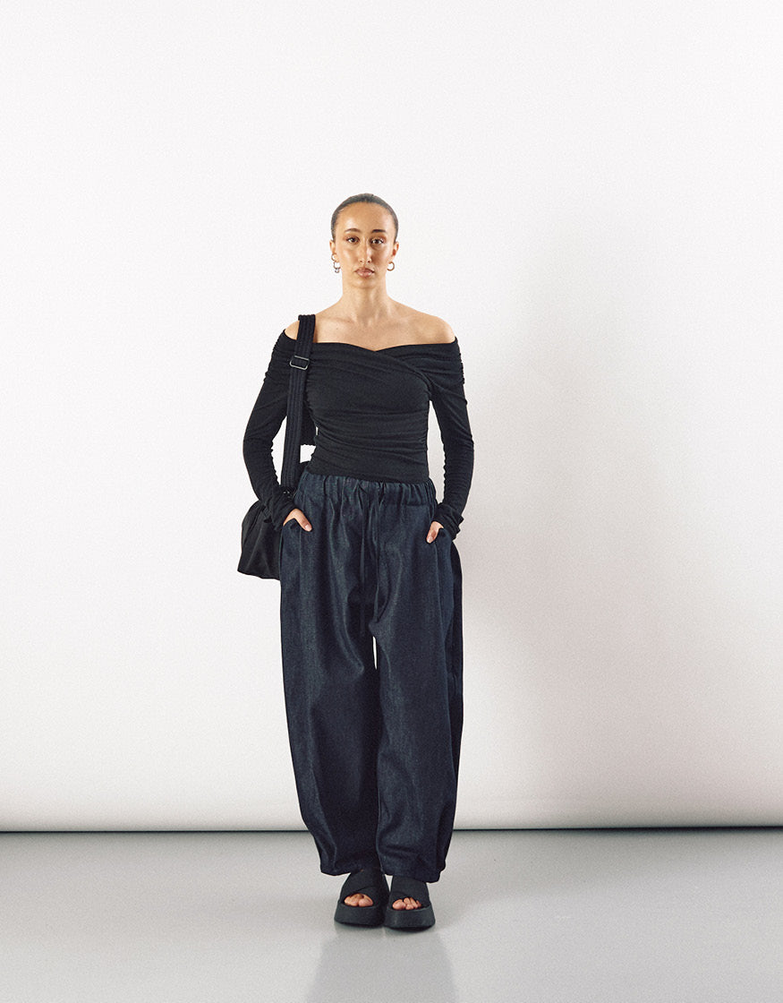 Female model wearing indigo wide-leg curved pants paired with a minimalist black off-shoulder top, showcasing relaxed volume and understated elegance.