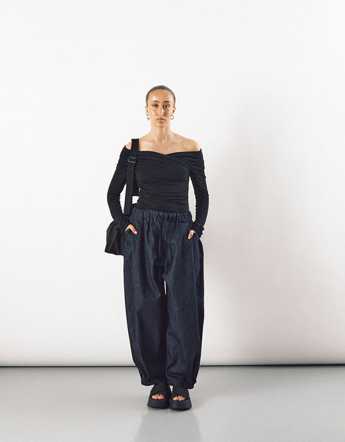 Female model wearing indigo wide-leg curved pants paired with a minimalist black off-shoulder top, showcasing relaxed volume and understated elegance.