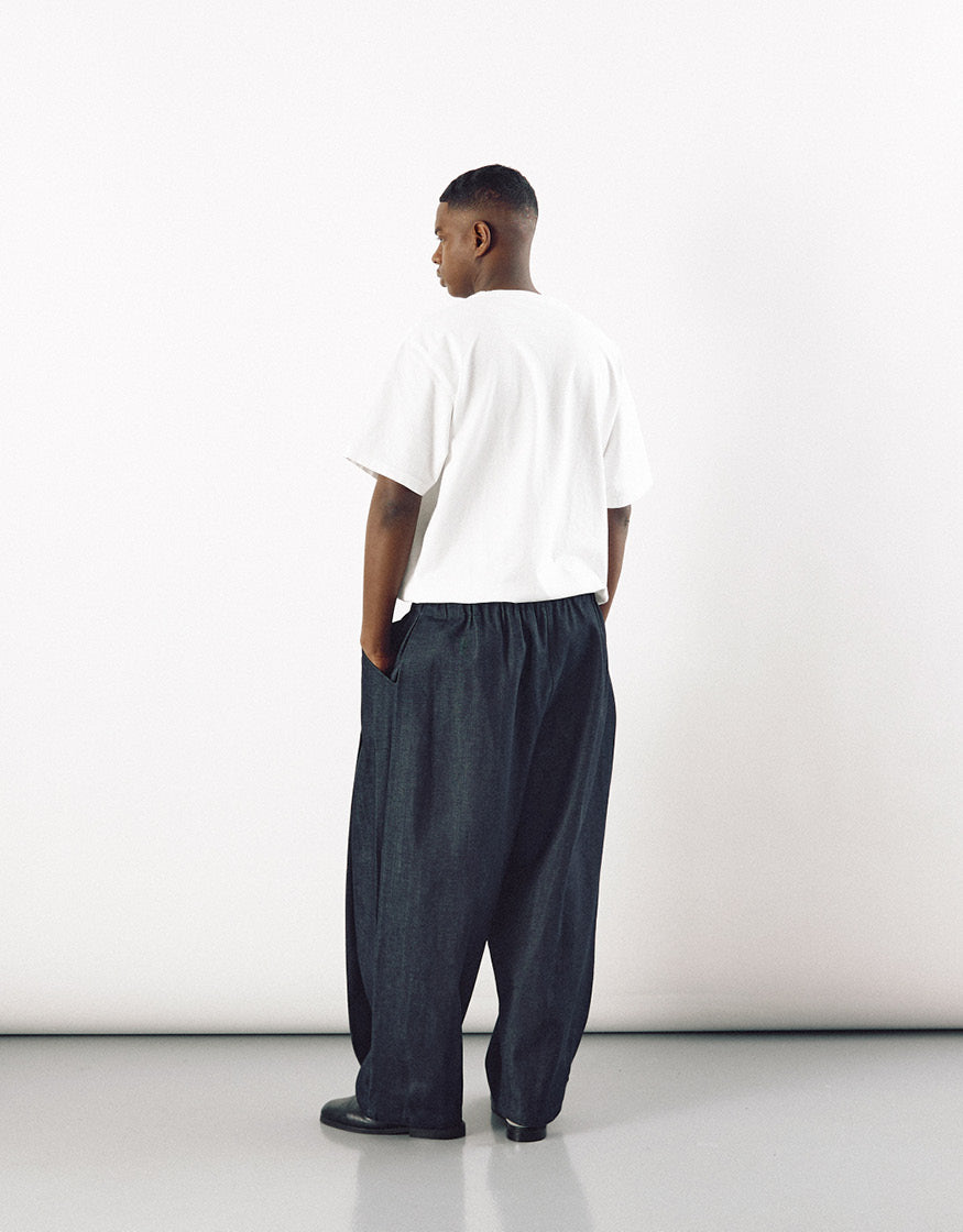 Man wearing relaxed fit indigo pants with a slight curve, paired with a simple white t-shirt, showcasing minimalist and understated design focused on comfort and movement.