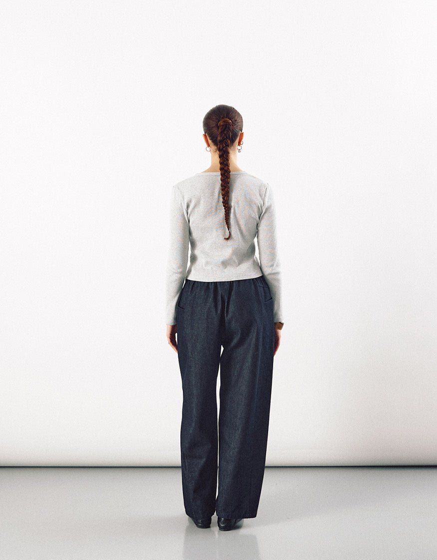 Back view of a person wearing indigo tapered pants with a relaxed fit and straight silhouette paired with a fitted light grey long-sleeve top against a plain background.