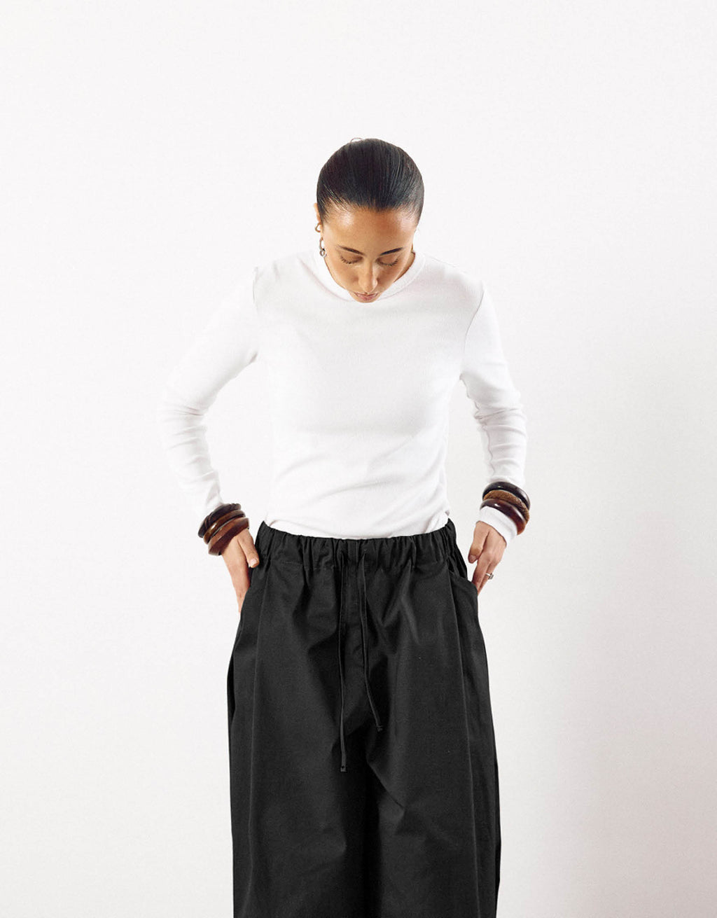 A minimalist look featuring black curved pants with a relaxed fit and gathered waist paired with a simple white long-sleeve top, emphasizing clean lines and understated elegance.