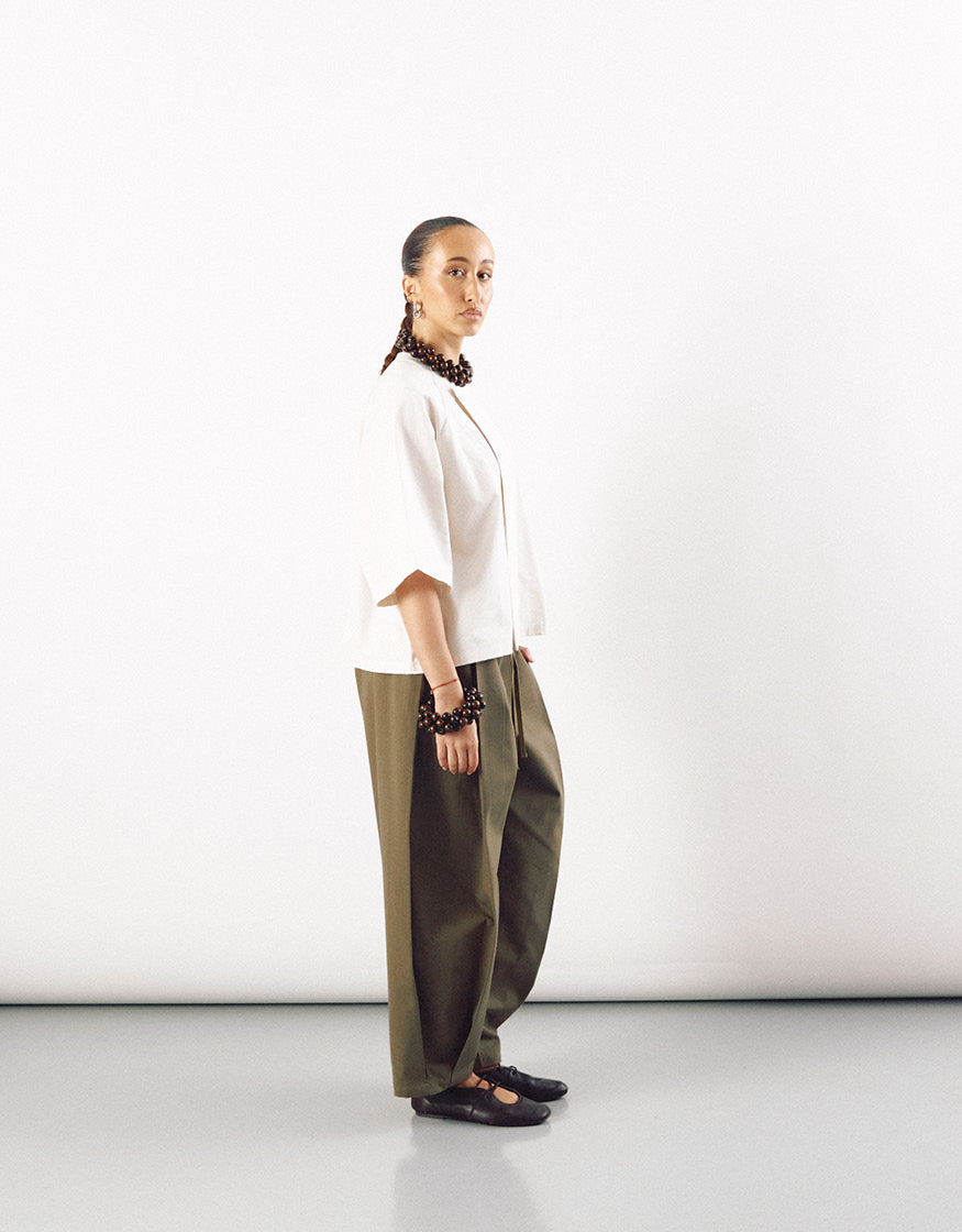 Side view of a model wearing an off-white short sleeve minimalist shirt paired with wide-leg olive green pants, styled with dark accessories and black shoes.