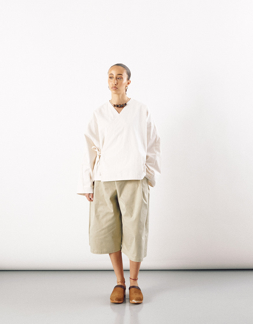 Model wearing wide, straight leg beige long shorts paired with an oversized minimalist cream top and brown slip-on shoes, highlighting understated elegance.